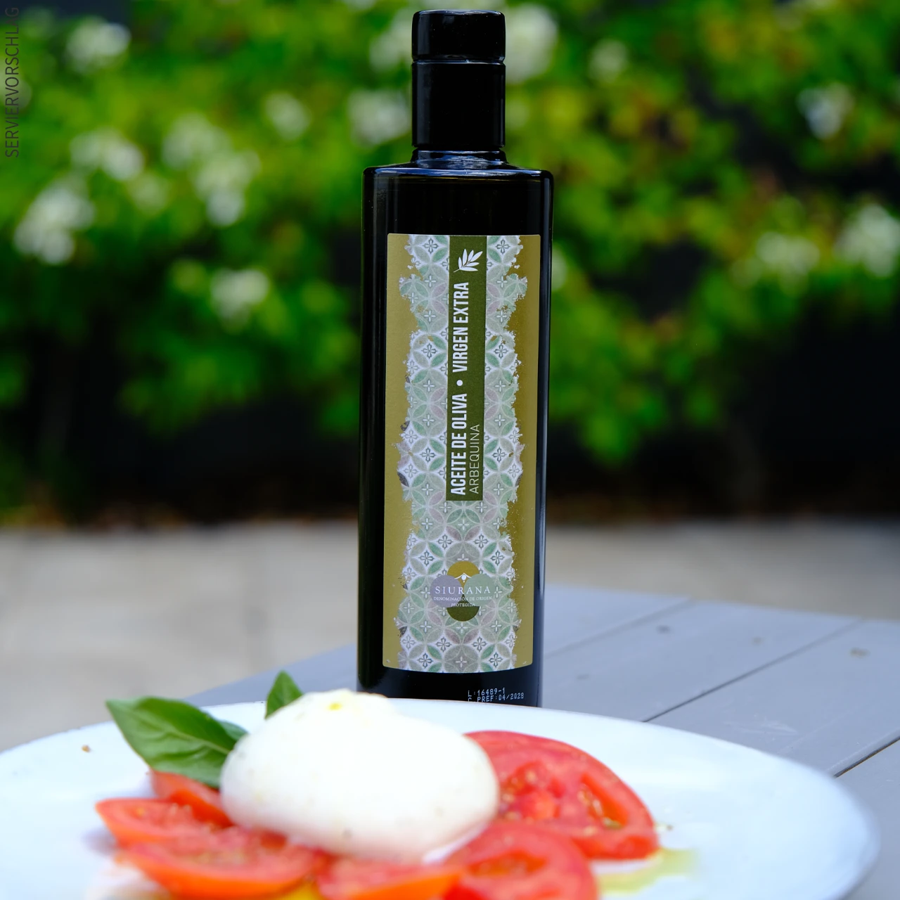 Hervorragenes Olivenöl zum Verfeinern von Speisen Eine Flasche Olivenöl und angerichteter Tomatensalat