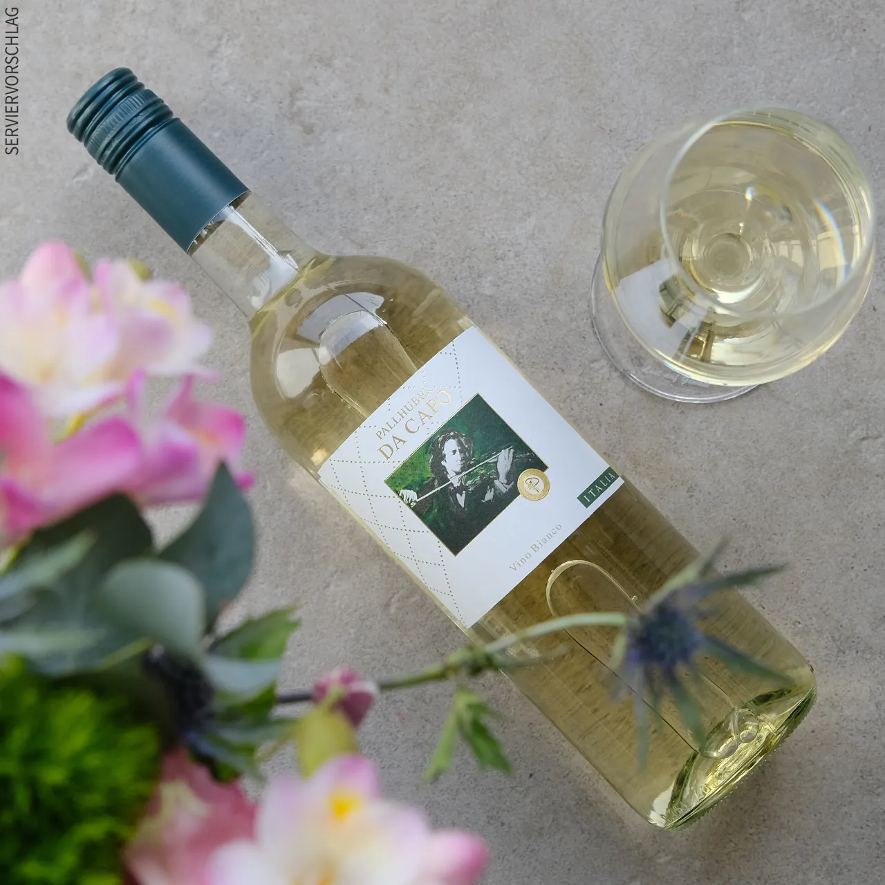 Eine Flasche Pallhuber Da Capo bianco, ein Glas Weißwein und ein sommerlicher Blumenstrauß