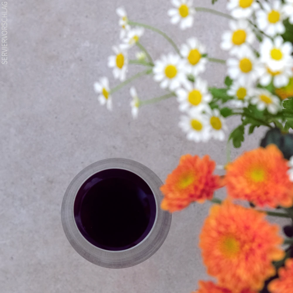 Ein Glas Jumi umgeben von orangenen Blumen und Kamille.
