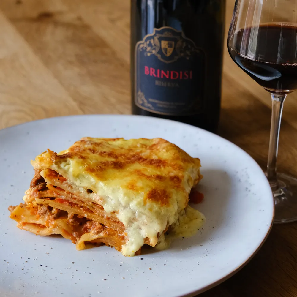 Rezept für eine klassische Lasagne Ein Stück Lasagne und ein Glas Brindisi Rotwein