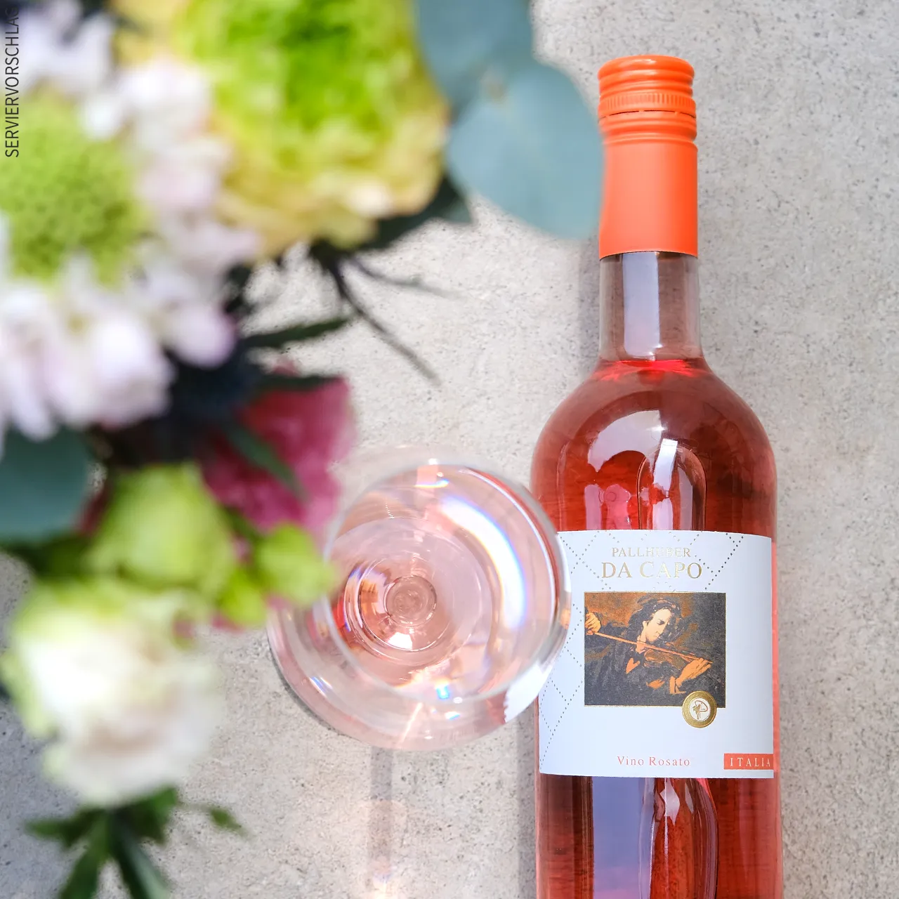 Eine Flasche Pallhuber Da Capo rosato und ein Glas mit dem Wein im Garten