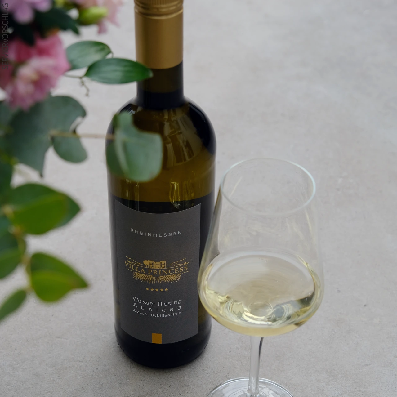 Nahaufnahme einer Flasche Weisser Riesling Auslese mit gefülltem Weinglas.